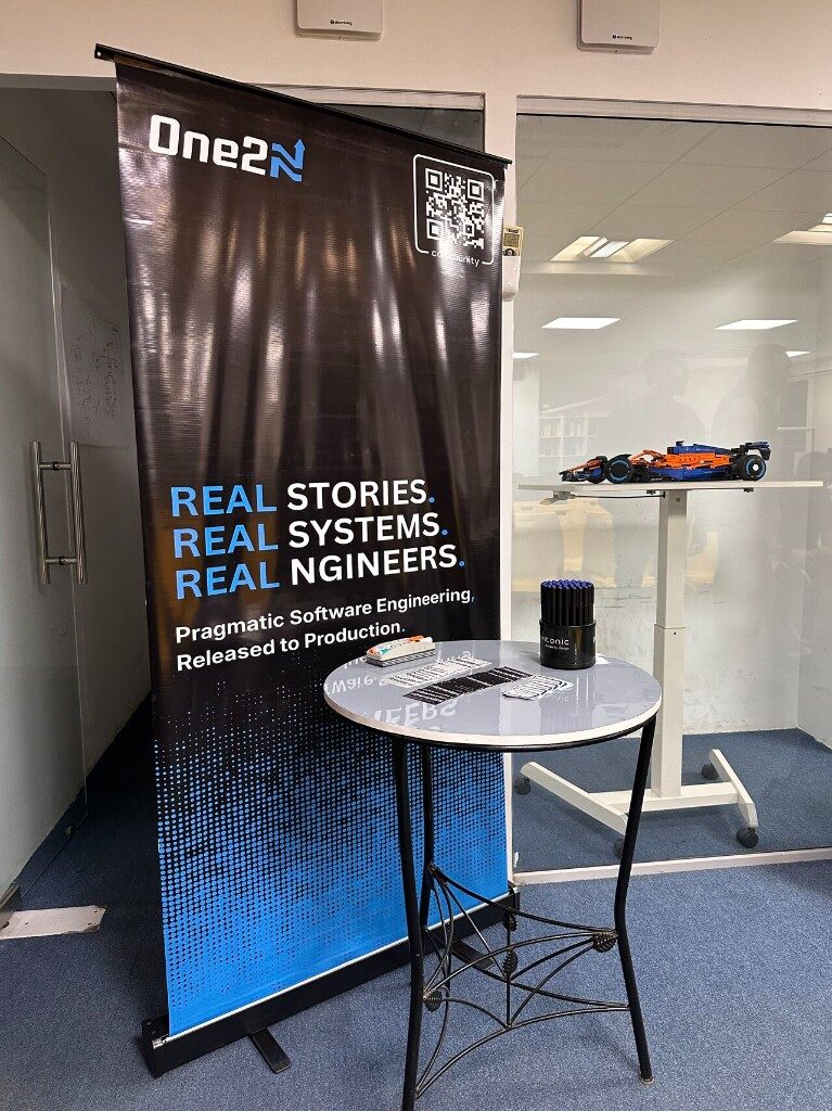 One2N banner – Real stories, real systems, real engineers – with promo table and model car, Episode 2